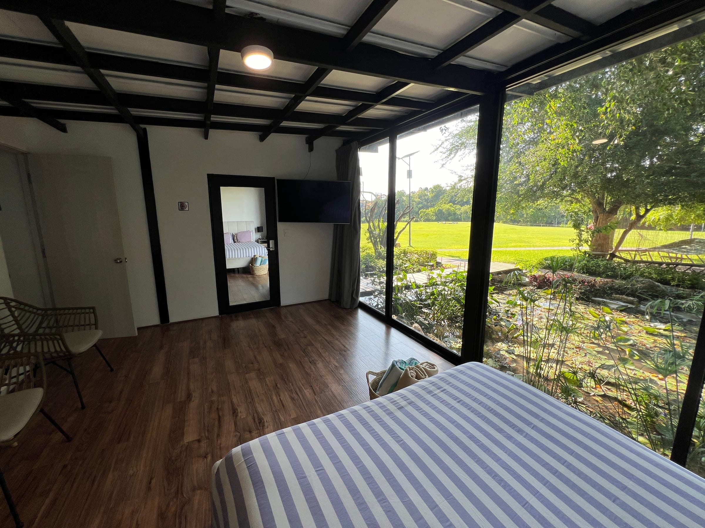 Interior de la habitación con TV y ventanales de piso a techo abiertos hacia el estanque y el jardín